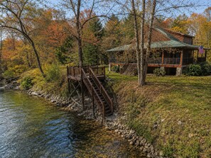 Une cabane dotée d’une terrasse en bois et d’un escalier en pierre menant à une plateforme surplombant une rivière.