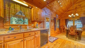 A wooden cabin interior with a kitchen and dining area, featuring wooden cabinets, a dishwasher, and a dining table with chairs.