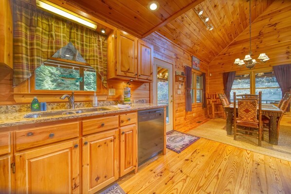 L’intérieur d’un chalet en bois comprend une cuisine et un coin repas, avec des meubles de rangement en bois, un lave-vaisselle et une table à manger avec des chaises.