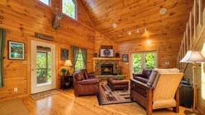 A log cabin interior with a fireplace, leather furniture, and a deer head mounted on the wall.