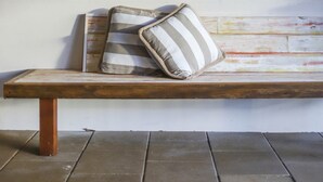 A wooden bench with two pillows against a white wall. - Seychelles Ground Level 2 Bedroom air-con self-contained apartment,  River views (Wooli)