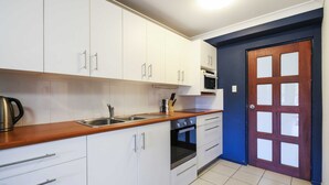 A kitchen with white cabinets, a wooden countertop, a sink, an oven, and a door with frosted glass panels. - Seychelles Ground Level 2 Bedroom air-con self-contained apartment,  River views (Wooli)