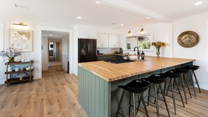 Een moderne keuken met een houten kookeiland, barstoelen en uitzicht op de woonkamer.