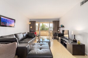 A modern living room with a leather sofa, a coffee table, a TV, and a desk with a lamp. - One Bedroom Condo Close to All the Action (Scottsdale)