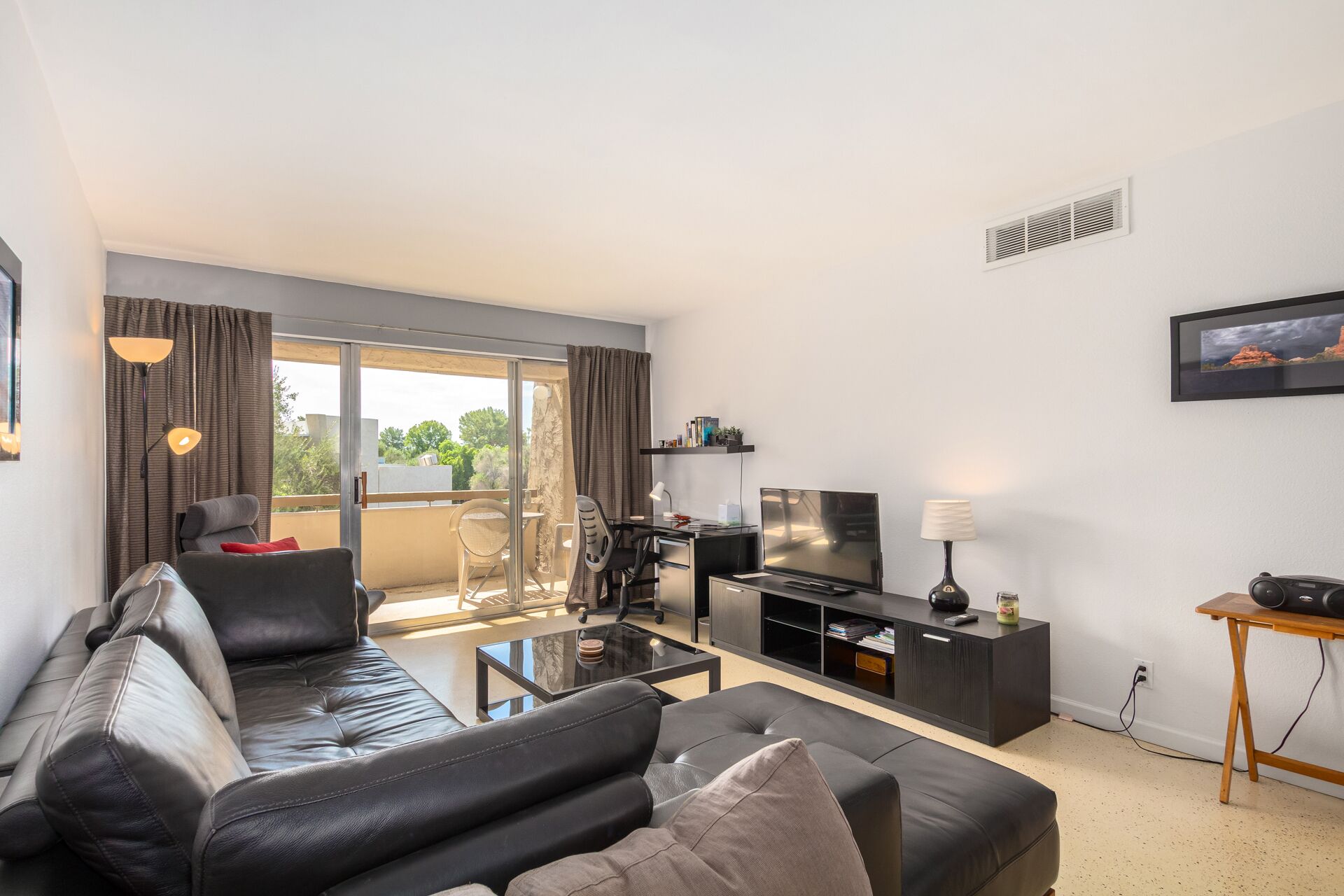 A modern living room with a black leather sofa, a glass coffee table, a TV, and a small side table.