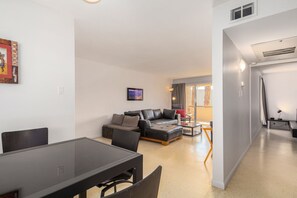 Relax in this stylish living area with a sofa set, dining table, and side table, offering a view of the outdoors through the large window.