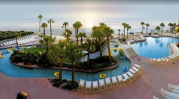 A pool area with lounge chairs and palm trees, surrounded by a pool deck.