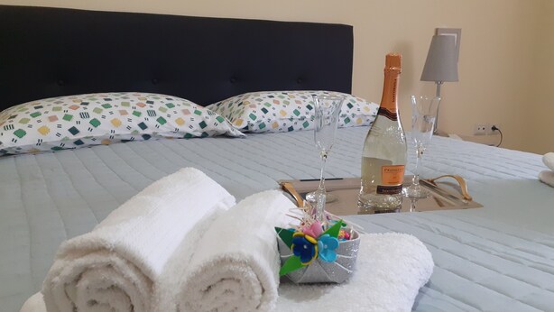A neatly made bed with rolled white towels, a bottle of Prosecco, and a decorative flower arrangement on a tray. - 500 mt from Porta Rudiae (Lecce)