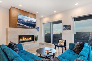 A modern living room with a fireplace, blue sofas, a coffee table, and a large TV.