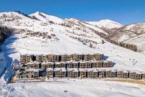 A snow-covered mountain with a row of multi-story buildings, likely a hotel, with a ski slope in the background.