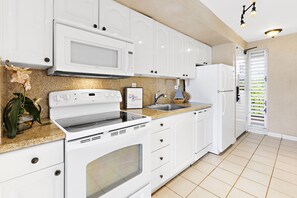 A kitchen with white appliances, a granite countertop, and a potted orchid. - 4th Floor Hawaiian hideaway in lush Kaanapali (Lahaina)