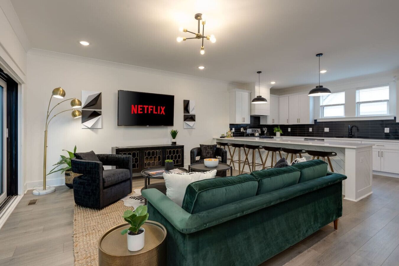 Un salon moderne avec un canapé vert, un téléviseur affichant le logo « NETFLIX » et un coin cuisine avec un bar.