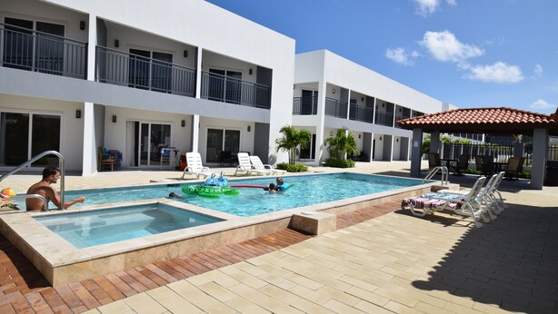A pool area with a rectangular pool, lounge chairs, and a covered seating area. - Flamboyan Condo Arena at Eagle Beach Aruba (Noord)