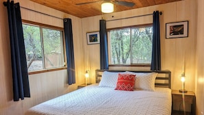 Ein Schlafzimmer mit Holzbalkendecke, einem Bett mit weißer Bettdecke, einem roten Kopfkissen und zwei Nachttischlampen sowie einem Deckenventilator.