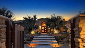 A pathway leading to a building with a decorative entrance, flanked by stone walls and palm trees.