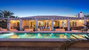 A poolside area with a covered seating area, a pool, and palm trees.