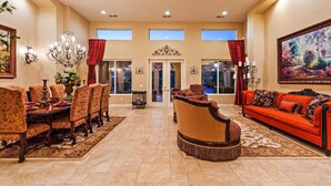A spacious living room with a dining area, featuring a chandelier, red curtains, and a large painting.