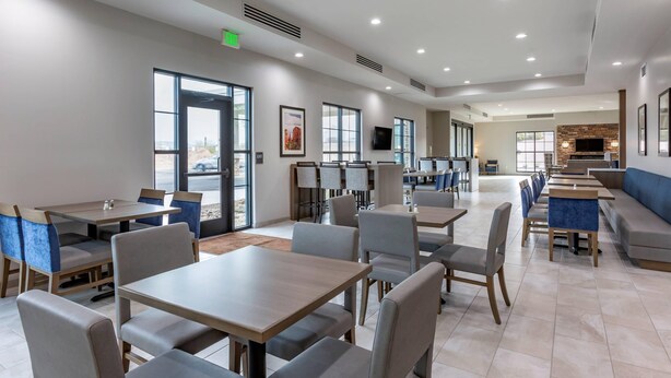 Ein geräumiger Essbereich mit mehreren Tischen und Stühlen, großen Fenstern und einem an der Wand befestigten Fernseher.