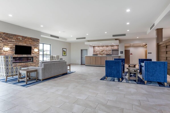 A modern hotel lobby with a fireplace, seating area, kitchen, and a large TV.