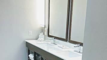 A bathroom with a white sink, a large mirror, and shelves below the sink holding towels.