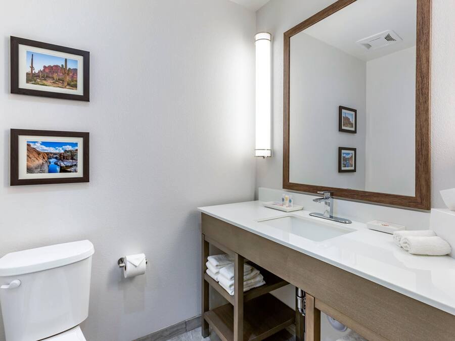 Un baño con un lavamanos blanco, un espejo y dos cuadros en la pared.