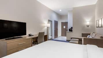 Een moderne hotelkamer met een groot bed, een bureau met een flatscreen televisie, een stoel, een bank en een kleine kitchenette.