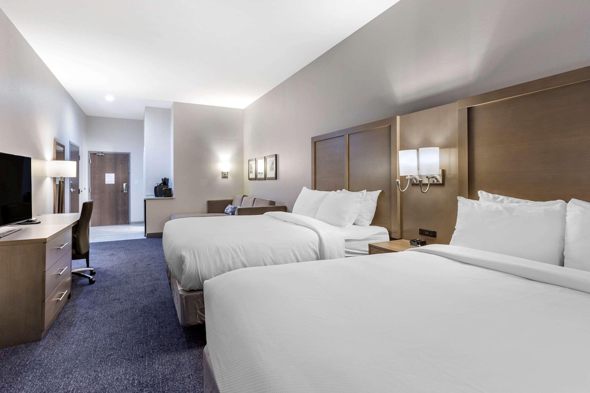 A hotel room with two beds, a desk, a chair, and a TV.