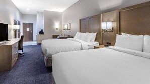 Ein Hotelzimmer mit zwei Betten, einem Schreibtisch mit Stuhl, einem Fernseher und einer Lampe.
