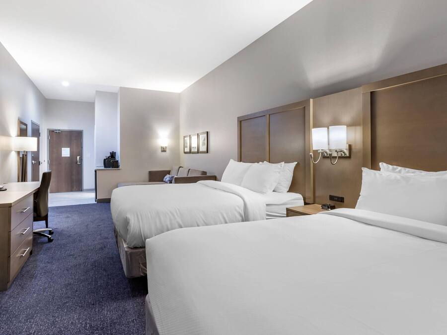 A hotel room with two beds, a desk with a chair, a TV, and a lamp.