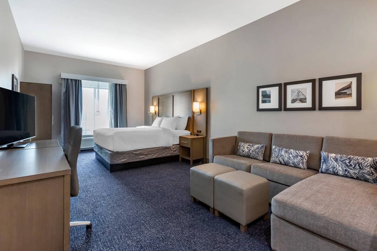 Een hotelkamer met een bed, een bureau, een televisie, een bank en een groot raam.