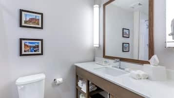 A modern bathroom with a white sink, mirror, and toilet. There are two framed pictures on the wall.