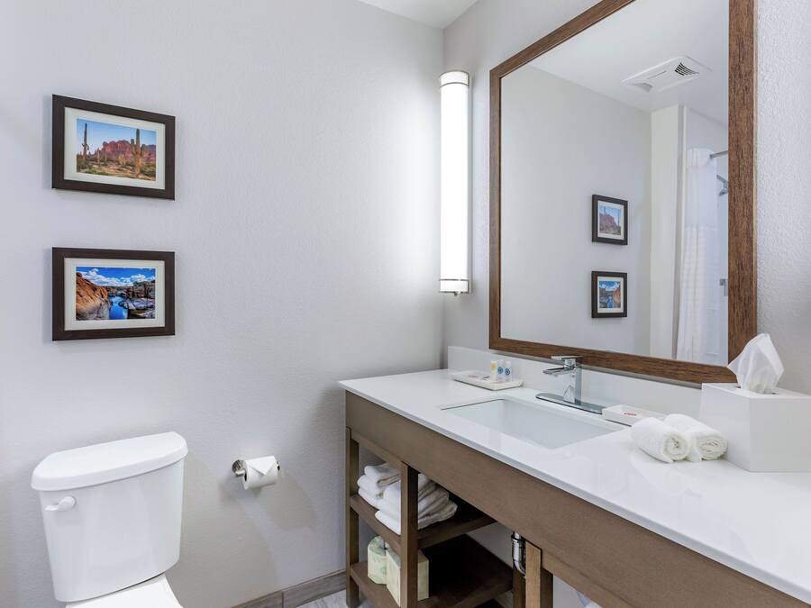 A modern bathroom with a white sink, mirror, and toilet. There are two framed pictures on the wall.