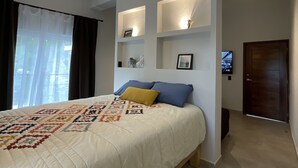 A bedroom with a bed, a hanging light fixture, a TV, and built-in shelving.