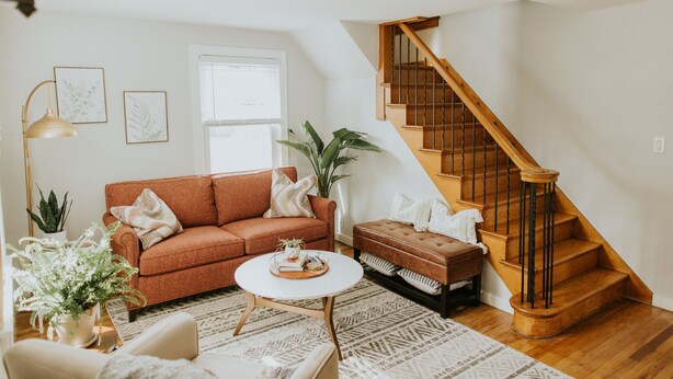 A living room with a brown sofa, a white coffee table, a staircase, and a potted plant. - The Franklin Green House in the heart of Berne, Indiana (Berne)