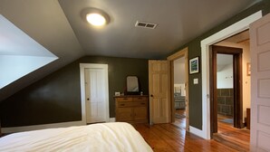 A bedroom with a sloped ceiling, a bed, a dresser, and a door leading to a bathroom.
