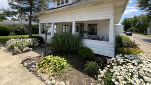 A single-story house with a covered porch, a small garden with flowers and plants, and a clear sky.
