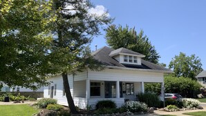 A single-story house with a front porch, a garage, and a small garden area with a lawn and a few plants.