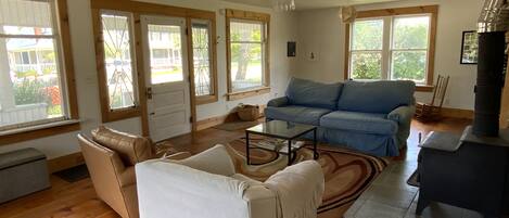 Amplia sala de estar con un sofá azul grande, un sillón blanco y una mesa de centro de vidrio. Cuenta con una chimenea y un ventanal que proporciona luz natural.