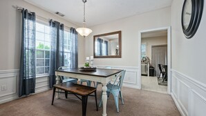 A dining area with a wooden table, blue chairs, a chandelier, and a mirror on the wall. - Pet-Friendly 3BR Home with Porch & Grill (Woodstock)