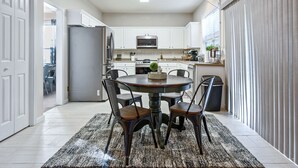 A modern kitchen with white cabinets, a central island, and a dining area with four chairs. - Pet-Friendly 3BR Home with Porch & Grill (Woodstock)