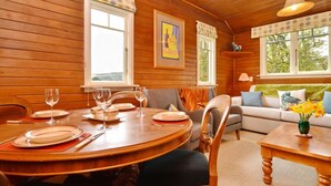 Un interior de madera con una mesa de comedor dispuesta para cuatro personas, un sofá y un ventanal con vistas a la vegetación.