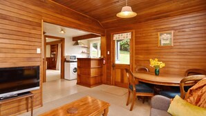 Un interior de cabaña acogedor, con una televisión, muebles de madera, una mesa de comedor con sillas y una zona de cocina.