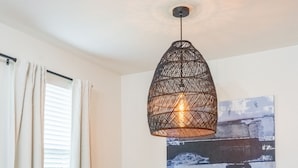 Et spiseområde med et bord, stole, en hængende lampe og et billede på væggen.
