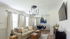 En moderne stue med sofa, sofabord og et spiseområde med stole.