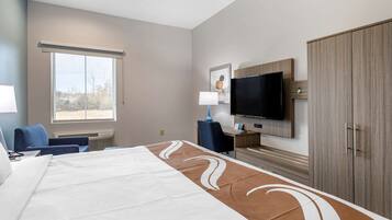 A hotel room with a large bed, a desk with a chair, a television, and a wardrobe.