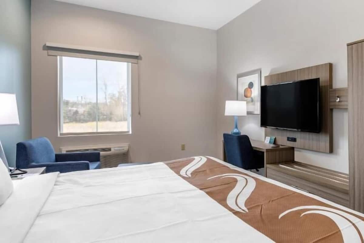 Ein Hotelzimmer mit einem großen Bett, einem Fernseher, einem Schreibtisch und einem Kleiderschrank.