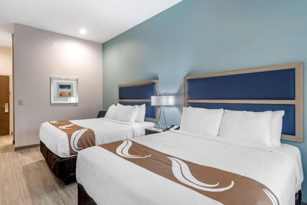 Ein Hotelzimmer mit zwei Betten, einem Nachttisch, einer Lampe und einem gerahmten Bild an der Wand.