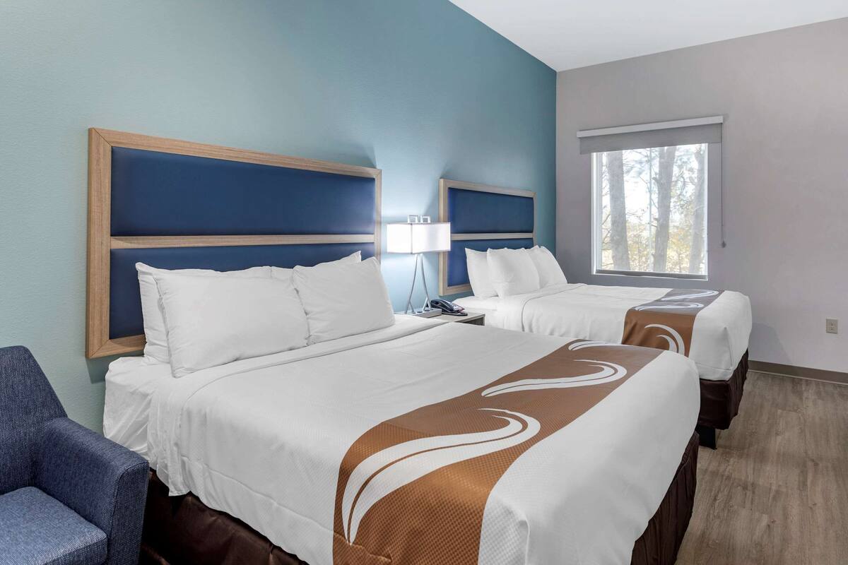Ein Hotelzimmer mit zwei Betten, einem Schreibtisch, einem Stuhl und einem Fenster.