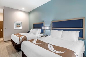 A hotel room with two beds, each with a headboard, a bedside table with a lamp, and a framed picture on the wall.