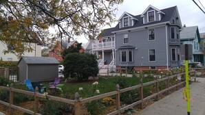 A two-story house with a front porch, a small shed, and a fenced garden area with various plants and flowers. - Davis Square Inn (Somerville)